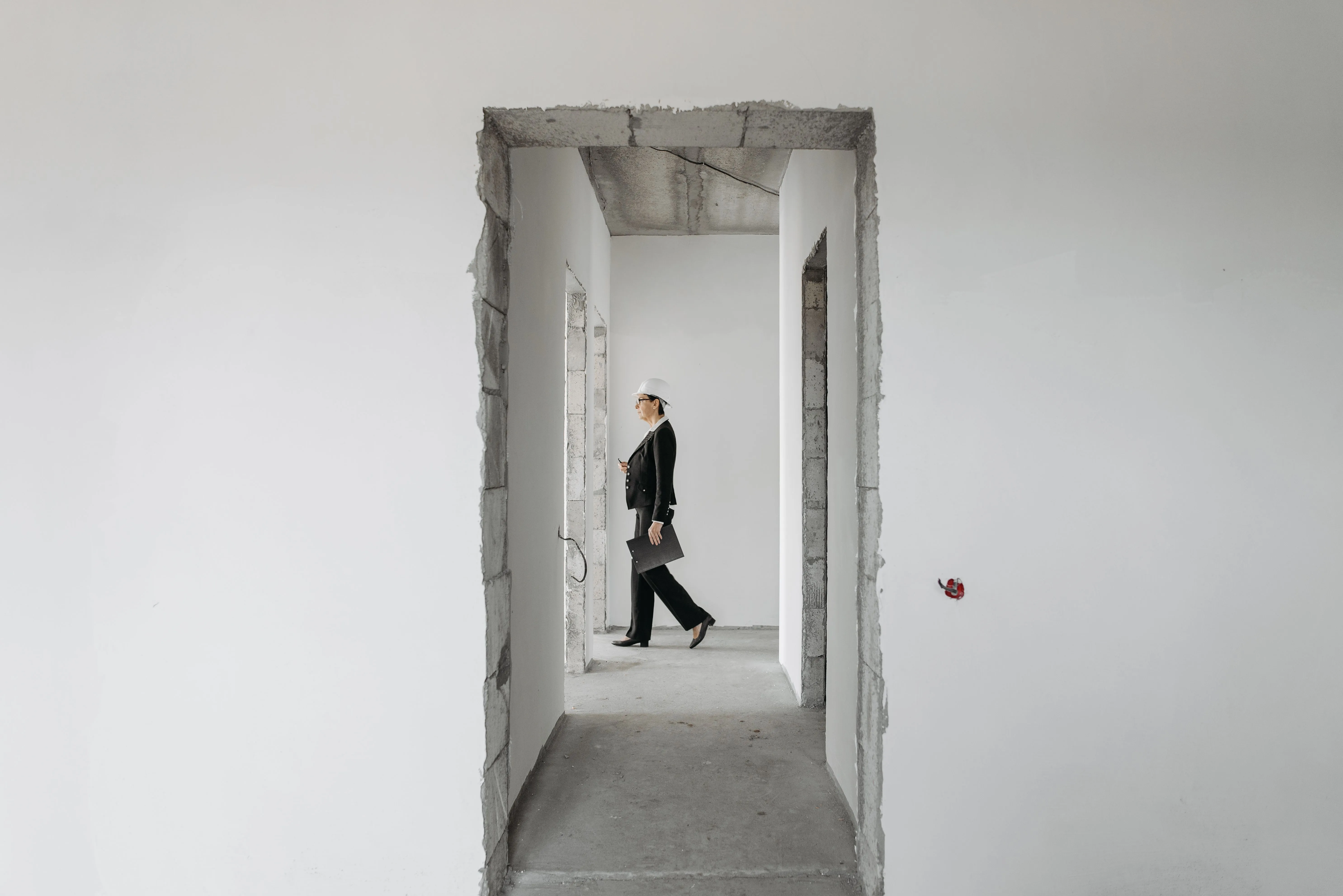 An inspector in a hard hat walking through an unfinished concrete interior.