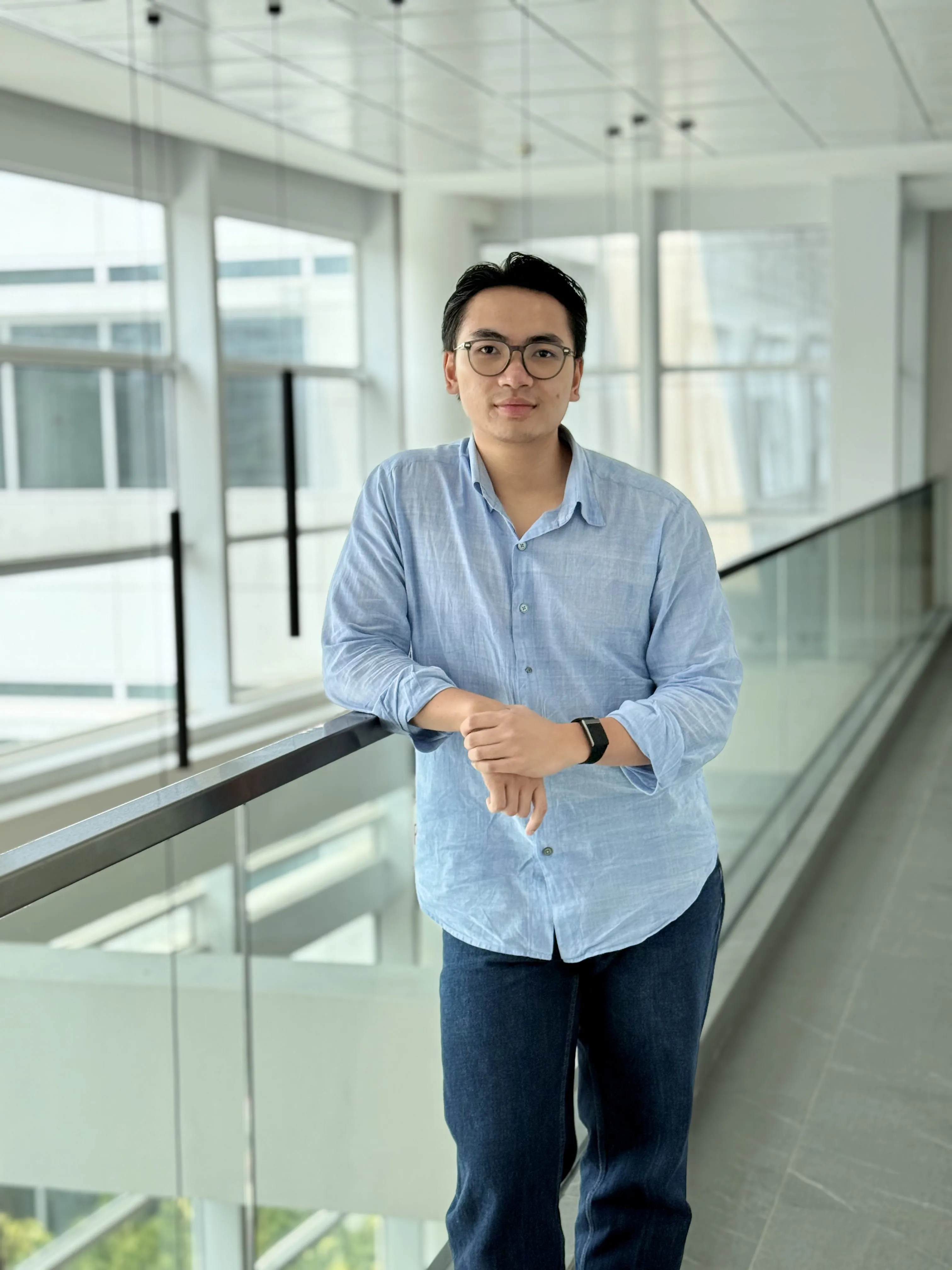 Keni Winata, standing at a glass balustrade in an office corridor.