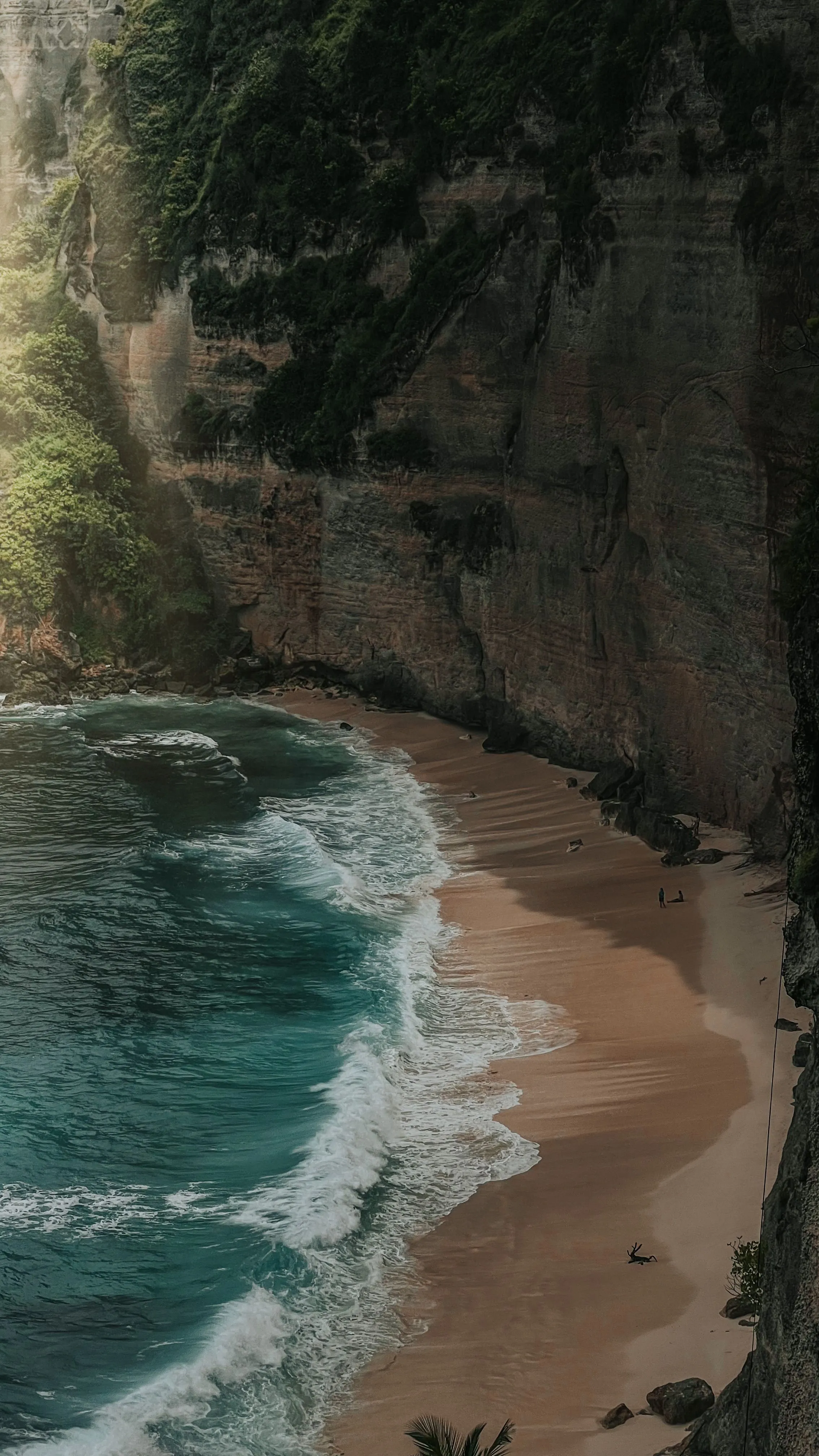 A sheltered cove beneath a cliff face, water drawing back from the sand.
