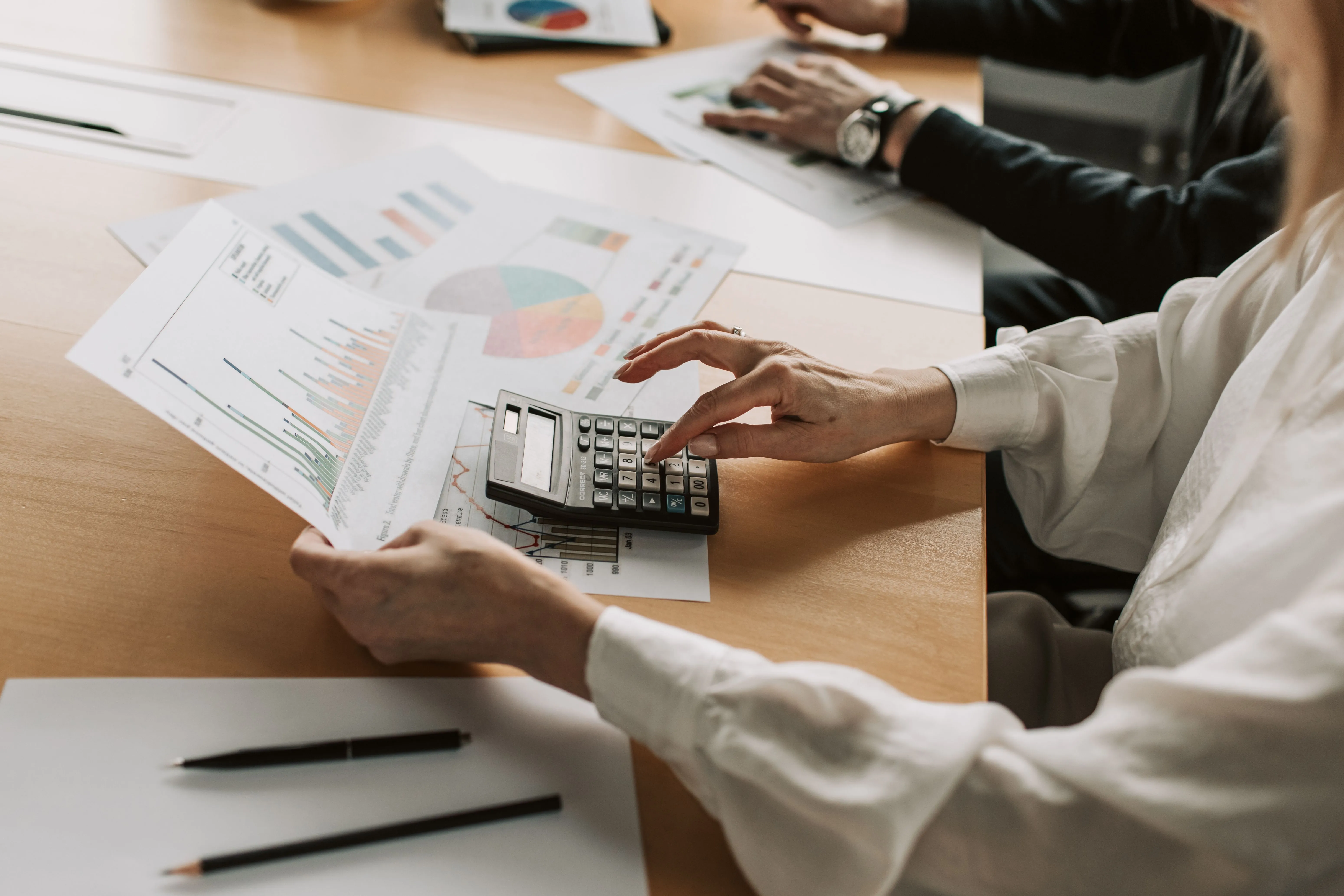 Two people reviewing printed charts and a calculator across a desk.